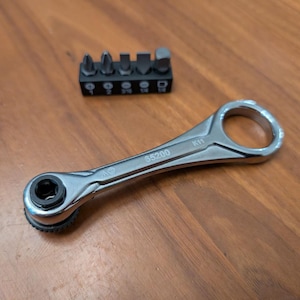 May include: A silver ratchet wrench with a black head and a set of black screwdriver bits. The wrench has the number "65200" printed on it. The screwdriver bits are in a black holder.