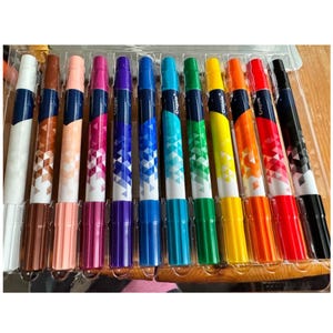 Puede incluir: Un juego de rotuladores Crayola en una bandeja de plástico transparente. Los rotuladores son de varios colores, incluyendo blanco, marrón, rosa, morado, azul, verde, amarillo, naranja, rojo y negro. Cada rotulador tiene un diseño geométrico.