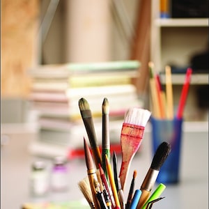 May include: A close-up of a ceramic jar filled with a variety of paintbrushes, including round, flat, and angled brushes. The brushes are in various sizes and colors, including black, brown, red, and green.