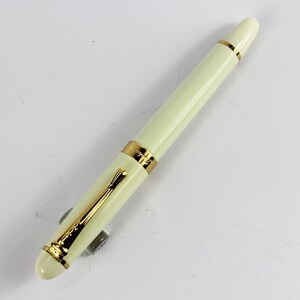 May include: A white fountain pen with gold accents. The pen has a cap and a clip.