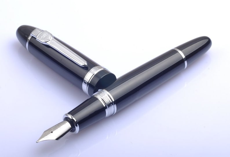 May include: A black fountain pen with silver accents and a fine nib. The pen is lying on a white surface.