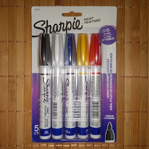 Könnte beinhalten: Eine Packung mit fünf Sharpie Öl-basierten Farbstiften in Schwarz, Weiß, Blau, Gelb und Rot. Die Stifte sind mit "Paint" und "Medium" beschriftet. Die Verpackung weist auch "Great for craft surfaces" aus.