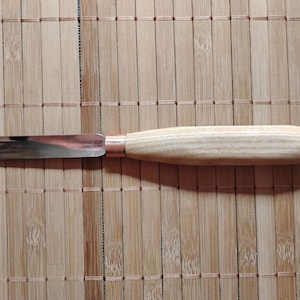Może przedstawiać: Narzędzie do rzeźbienia z drewnianym uchwytem i metalowym ostrzem. Narzędzie leży na bambusowej macie.