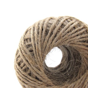 May include: A close-up of a roll of natural twine, a type of string made from natural fibers, wound into a tight coil. The twine is a light brown color and has a rough texture.