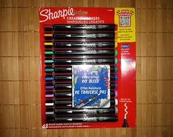 May include: A pack of 12 Sharpie Creative Markers with a red background. The markers are water-based acrylic and have a bullet tip. The packaging features the text "Paint Effect No Bleed" and "Effet Peinture Ne Traverse Pas".