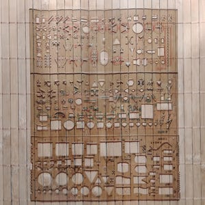 May include: A set of two brown plastic stencils with various shapes and sizes, including circles, squares, triangles, and rectangles. The stencils are designed for use with a pencil or pen to create patterns and designs.