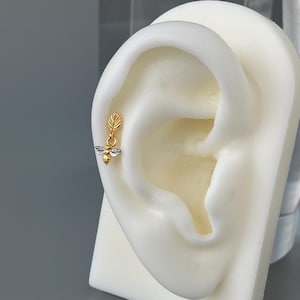 May include: Gold and silver bee charm dangling from a gold leaf on a cartilage earring.