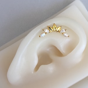 Könnte beinhalten: Goldener Ohrring mit einer Reihe von markisenförmigen, klaren Steinen und einem Blattdesign.