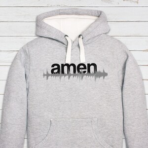 May include: A gray hooded sweatshirt with a white interior lining. The sweatshirt has a black print of the word "amen" with a sound wave graphic underneath.