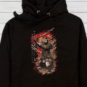 May include: Black hooded sweatshirt with a graphic print of a warrior holding a sword in a red and brown color scheme. The graphic includes Japanese text.