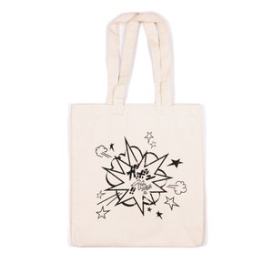 以下が含まれることがあります： 白いキャンバス地のトートバッグに、星と「KABOOM!」の文字が書かれた、漫画風の爆発の黒いプリントが施されています。
