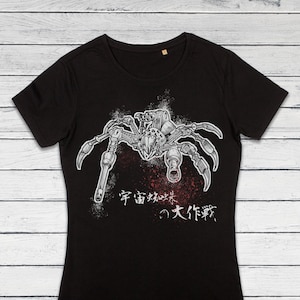Könnte beinhalten: Schwarzes T-Shirt mit einem weißen Grafikdruck einer Roboter-Spinne mit Waffen. Der Text "宇宙 賊 襲来 の 大 作戦" ist unter der Spinne gedruckt.