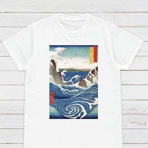 May include: White t-shirt with a blue and white print of a Japanese wave design. The print features a large wave with a swirling pattern and a mountain in the background. The text "神奈川沖浪裏" is printed in red on the right side of the print.