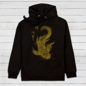 May include: Black hooded sweatshirt with a gold graphic of a koi fish and Japanese text that reads "真の強さ" (ma no tsuyosa) which translates to "True Strength".