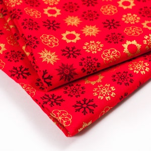 May include: Red fabric with a gold snowflake pattern. The fabric is folded in half, showing the pattern on both sides.