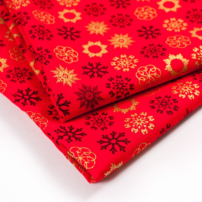 May include: Red fabric with a gold snowflake pattern. The fabric is folded in half, showing the pattern on both sides.