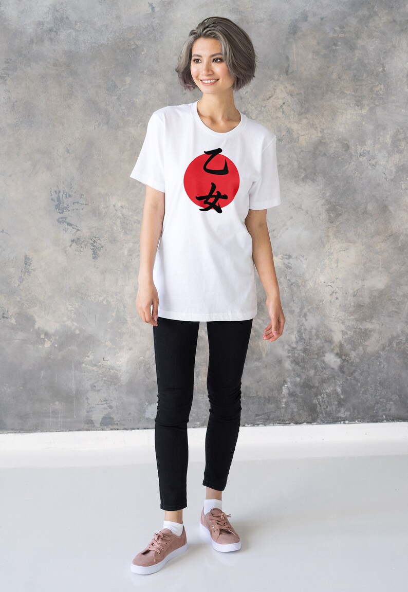 May include: A white t-shirt with a red circle and black Japanese characters that say "乙 女" on the front. The person wearing the shirt is standing in front of a gray concrete wall.