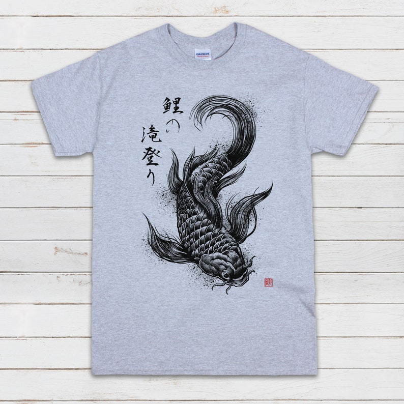 K&ouml;nnte beinhalten: Ein graues T-Shirt mit einer Schwarzwei&szlig;illustration eines Koi-Karpfens und japanischer Kalligraphie, die "躍" (Sprung) "志" (Ehrgeiz) "高く" (hoch) lautet.