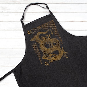 May include: Black denim apron featuring a gold dragon design. The dragon is curled up and has a detailed design.