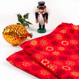 May include: Two red fabric napkins with a gold snowflake pattern and black snowflakes. A wooden nutcracker doll stands in the background.