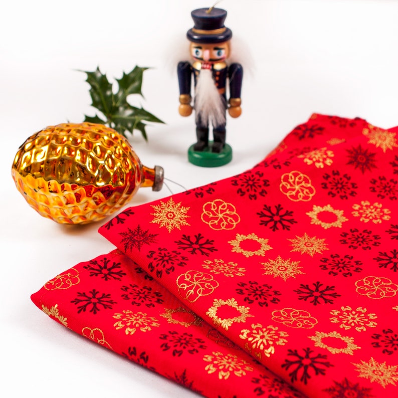May include: Two red fabric napkins with a gold snowflake pattern and black snowflakes. A wooden nutcracker doll stands in the background.