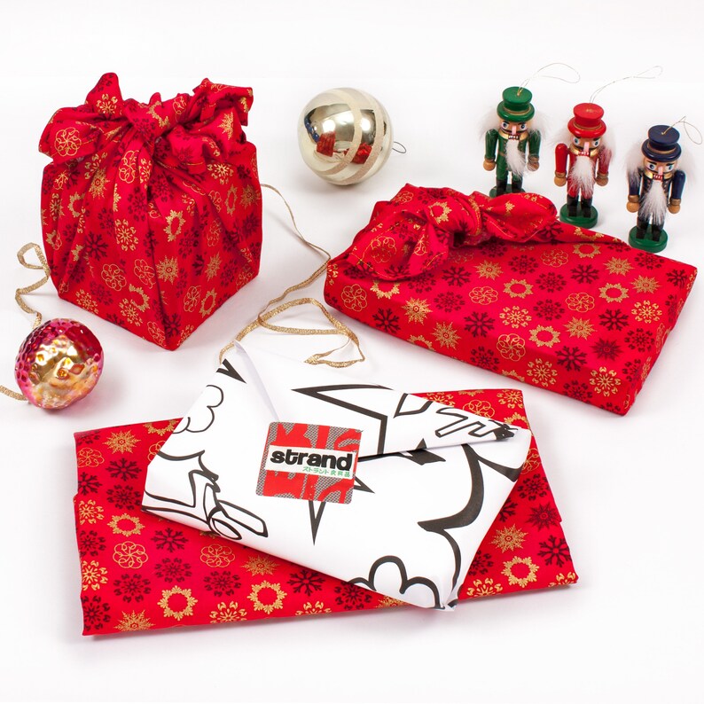 May include: A collection of red and gold patterned gift wrap with a white gift wrap with the word "strand" printed on it. There are also three nutcracker figurines with red, green, and blue accents.