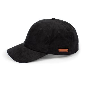 Puede incluir: Una gorra de béisbol de pana negra con un parche de cuero marrón en el lateral.