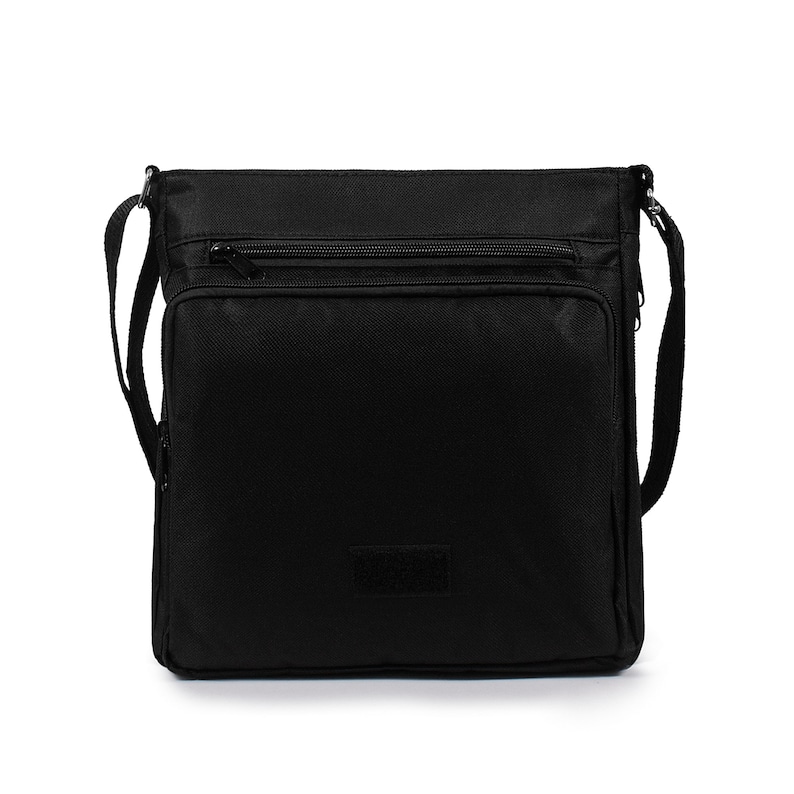 May include: A black square-shaped crossbody bag made of durable fabric. It features a main compartment with a zipper closure, a front zippered pocket, and an adjustable shoulder strap attached to the sides. A small rectangular patch is centered.
