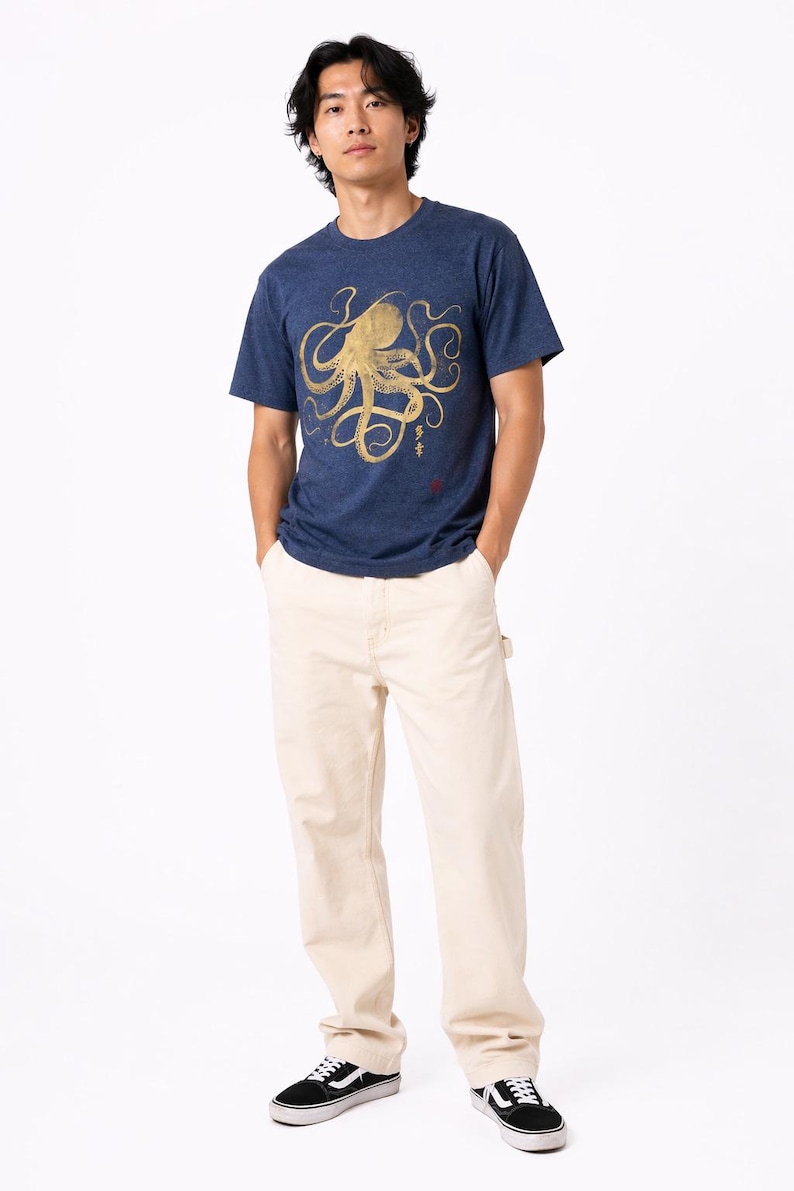 Pode incluir: Uma pessoa vestindo uma camiseta azul marinho com um desenho de polvo dourado e cal&ccedil;as cor creme. A camiseta tem gola redonda e mangas curtas. A pessoa tamb&eacute;m est&aacute; usando t&ecirc;nis preto e branco.