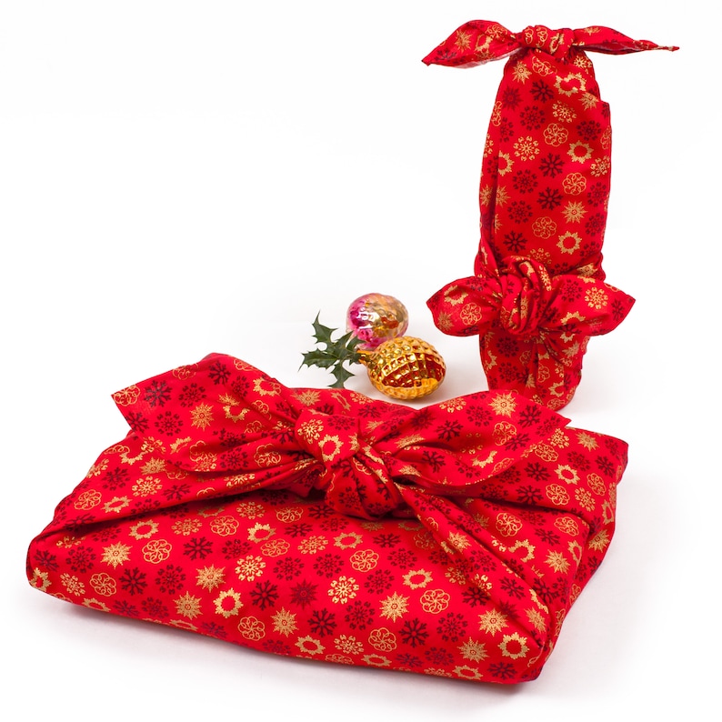 May include: Two red fabric gift boxes with gold snowflake patterns. The boxes are tied with a bow and are decorated with gold and red ornaments.
