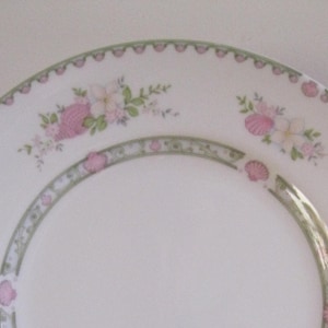 Peut inclure: Ensemble de quatre assiettes plates en céramique blanche avec un motif floral délicat dans des tons de rose et de vert. Les assiettes ont un bord festonné et un rebord surélevé.
