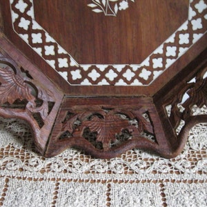 Peut inclure: Plateau octogonal en bois avec des sculptures complexes et un motif d'incrustation blanc. Le plateau a un bord festonné et est fait de bois foncé.