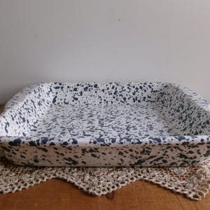 May include: A white ceramic baking dish with a speckled blue and white glaze. The dish has a rectangular shape with slightly rounded edges.
