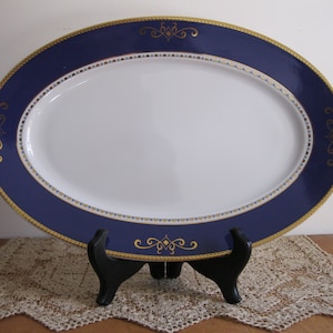 Peut inclure: Un plat de service ovale avec un centre blanc et un large bord bleu avec des accents dorés. Le bord présente un motif décoratif de volutes dorées et de points.