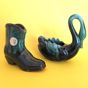 May include: Two ceramic planters, one shaped like a cowboy boot and the other shaped like a swan. Both planters are glazed in a dark green and black colour scheme.