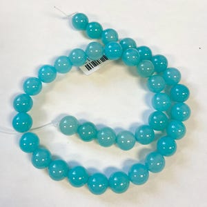 Op de afbeelding: Een streng ronde turquoise blauwe kralen. De kralen zijn glad en hebben een lichte glans.