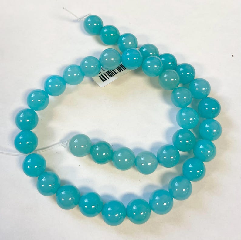 Op de afbeelding: Een streng ronde turquoise blauwe kralen. De kralen zijn glad en hebben een lichte glans.