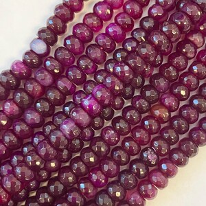 May include: Close-up of several strands of faceted, deep purple gemstone beads. The beads have a multifaceted cut, creating a sparkling effect. The color varies from a deep burgundy to a vibrant magenta, with a polished finish. Ideal for jewelry making.