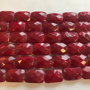 May include: A strand of red faceted glass beads. The beads are rectangular in shape and have a glossy finish.