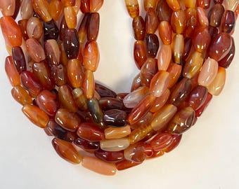 Puede incluir: Una hebra de cuentas de cornalina, con una mezcla de tonos rojos, naranjas y marrones. Las cuentas son lisas y pulidas, con un aspecto natural y orgánico.
