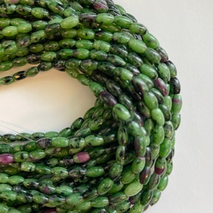 May include: A strand of green and black oval-shaped gemstone beads. The beads have a speckled pattern and some have a hint of purple.