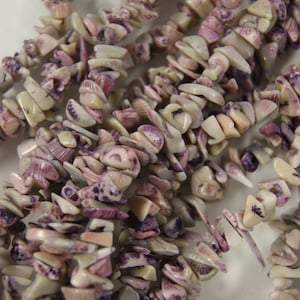 May include: A strand of purple and white shell beads. The beads are irregular in shape and size, and have a natural, organic look.