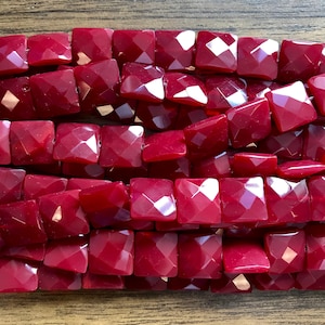 May include: A strand of red faceted square beads. The beads are made of glass and have a glossy finish.