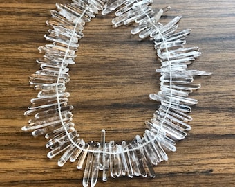 Pode incluir: Uma corda de pontas de cristal de quartzo transparente enfiadas em um fio branco. As pontas têm comprimentos variados e um acabamento natural e bruto.
