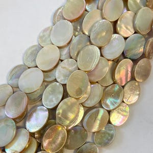 May include: A collection of iridescent, oval-shaped mother-of-pearl beads. The beads have a creamy white base color with shimmering, colorful highlights. The beads are arranged in a close-up, slightly angled view.