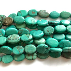 May include: A close-up of a pile of oval-shaped turquoise beads. The beads are a light blue-green color with brown veining.