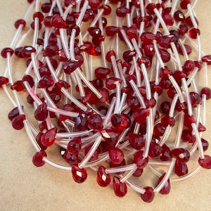 May include: A strand of red gemstone beads strung on clear elastic cord. The beads are faceted and have a teardrop shape.