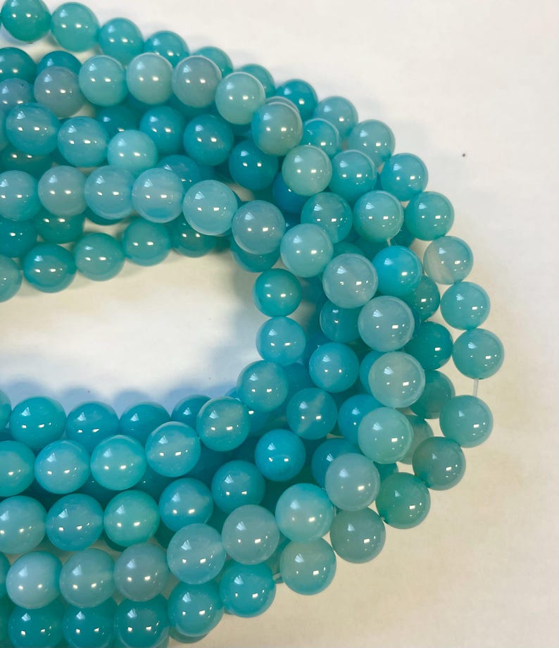 Op de afbeelding: Een streng ronde turquoise blauwe edelsteen kralen. De kralen zijn glad en hebben een lichte glans.