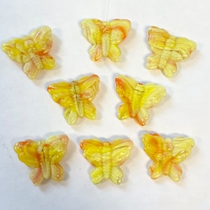 Puede incluir: Ocho cuentas de vidrio de mariposa amarillas y naranjas. Las cuentas son translúcidas y tienen un patrón de remolino.