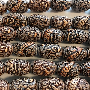 May include: A strand of brown and white carved wooden beads with a mermaid design. Each bead features a detailed carving of a mermaid with flowing hair and a fish tail.